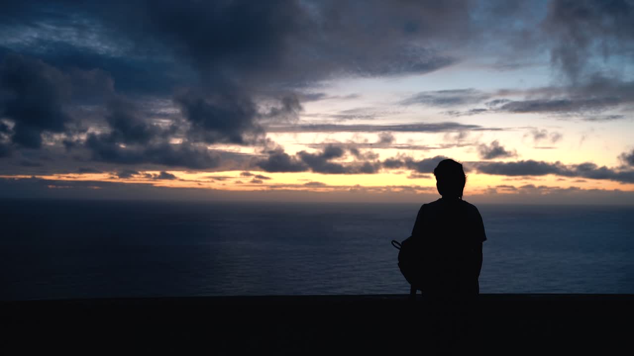 silueta de una mujer joven viendo una puesta de sol sobre el océano, toma media