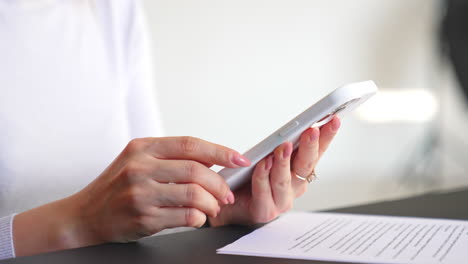 Female manicured hands hold the telephone. Lady presses some buttons on white phone at white backdrop. Close up.