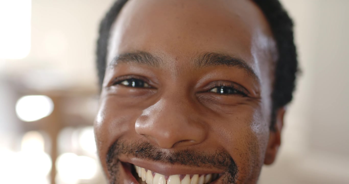 Afroamerikansk mand i 20'erne reagerer på en off-camera prompt, smiler og griner nær vindueslys