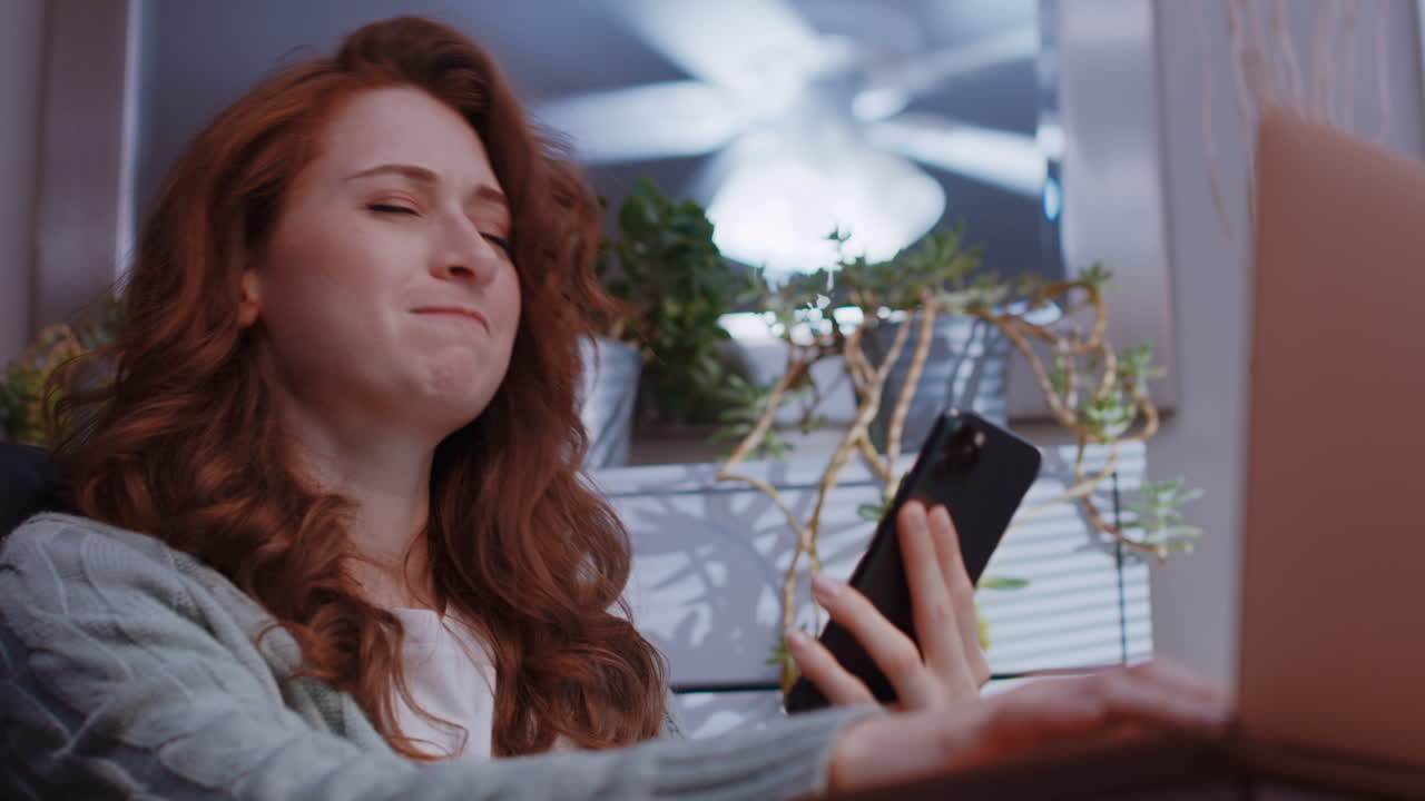 una joven mujer caucásica está trabajando desde casa en su computadora portátil, recibe algunas malas noticias