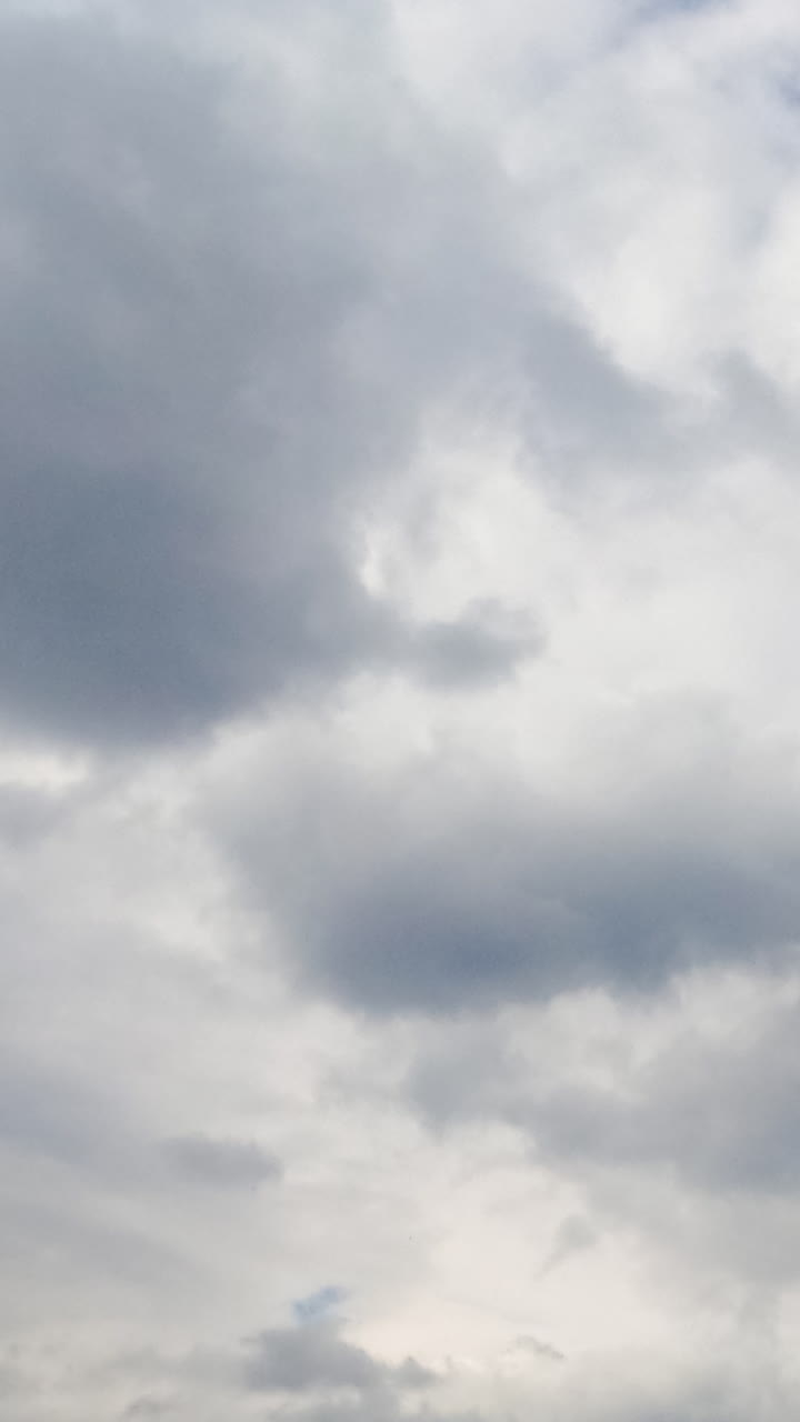 Azure sky hardly ever seen behind the grey cloudscape. Grey clouds accumulating in the atmosphere. Low angle view. Timelapse. Vertical video