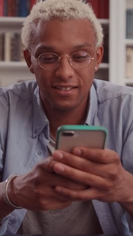 young positive african american man student uses mobile phone and writes sms