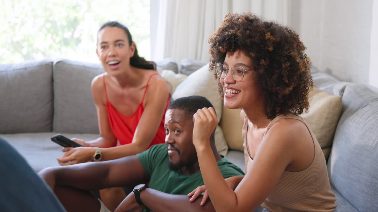 Diverse friends relaxing on sofa, enjoying conversation and laughter at home