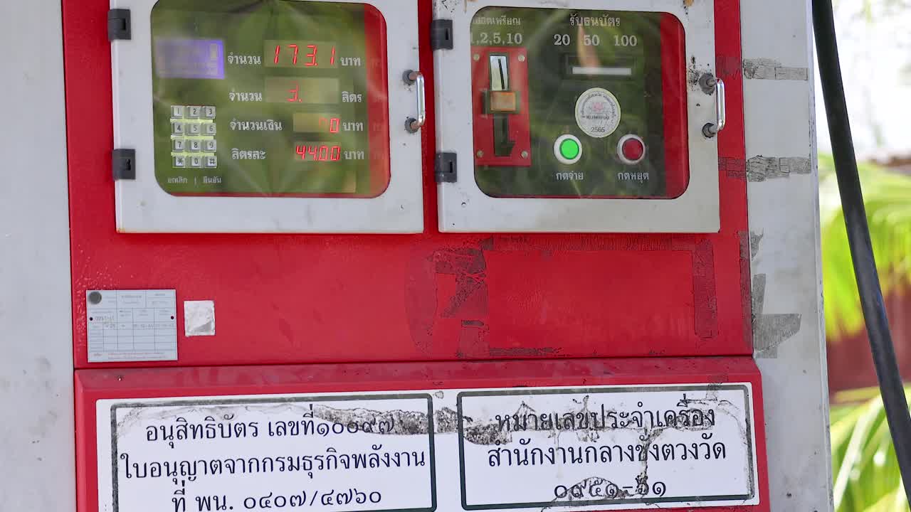 A red coin-operated fuel dispenser in Phuket, Thailand, under bright daylight, displaying instructions and fuel type labels