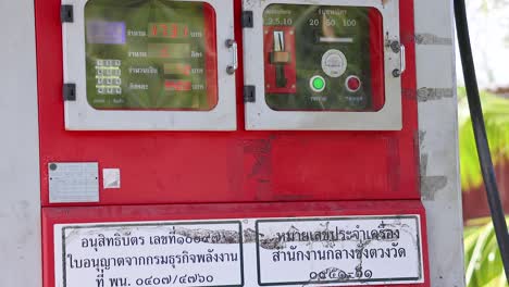 a red coin-operated fuel dispenser in phuket, thailand, under bright daylight, displaying instructions and fuel type labels