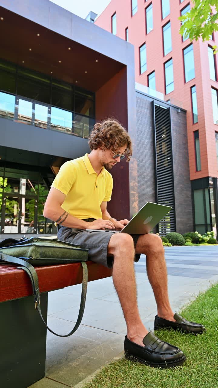 Man in yellow shirt talking standing on a bench and working on a laptop. Vertical