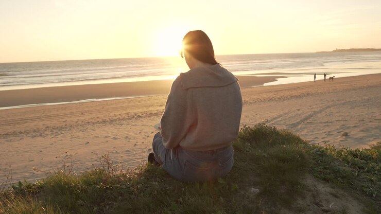 Traveling woman sitting on hill against sunset sky near sea