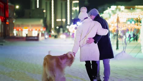 couple walking a dog in a snowy city at night