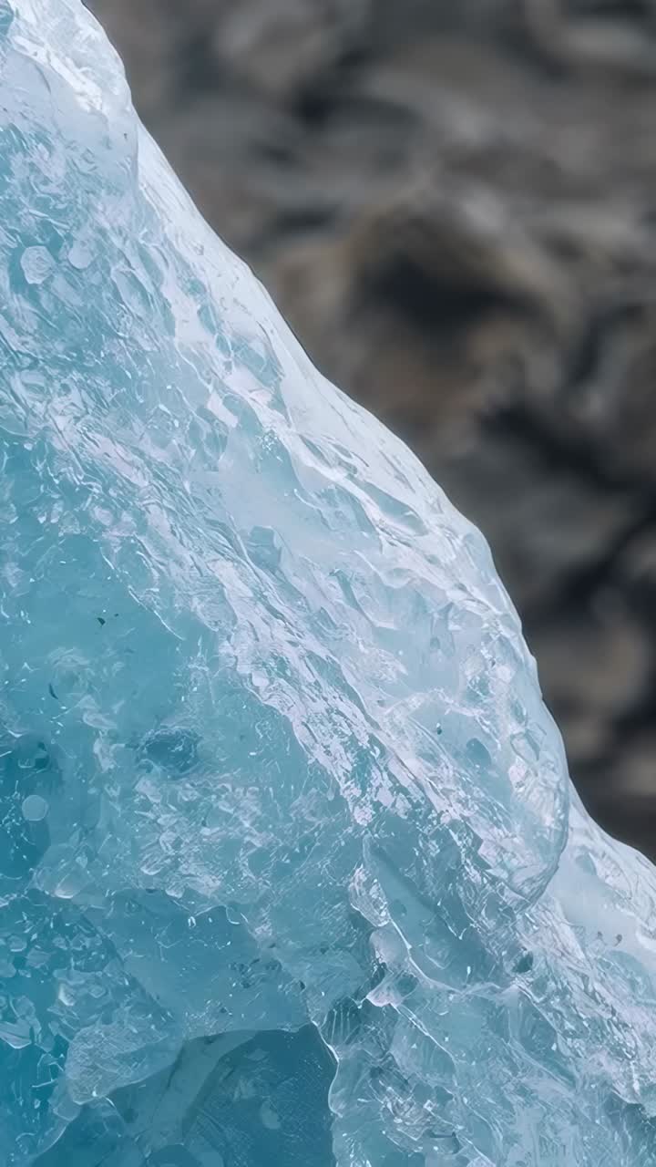 Video verticale: una telecamera riprende il ghiaccio glaciale blu che riempie la parte sinistra dell'inquadratura, accanto a una roccia scura che mostra delle bolle