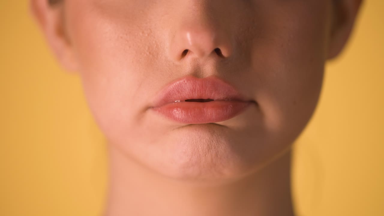primer plano extremo de los labios de una mujer hermosa mientras hace que sus labios revolotean porque algo es agotador o imposible frente al fondo amarillo en cámara lenta