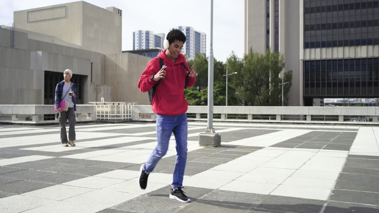 Asian male hearing beat on headphones adjusting backpack, moving on rooftop terrace with smartphone