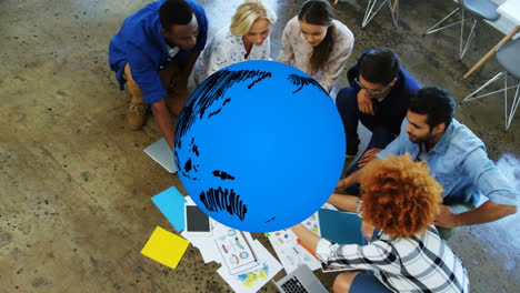 animation of blue globe rotating over diverse creative colleagues brainstorming on office floor