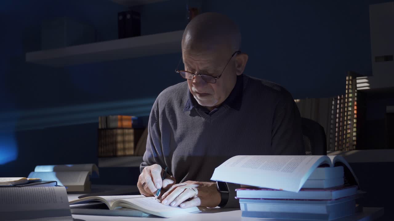 Researcher or historian mature old man reading a book, taking notes while studying at home.