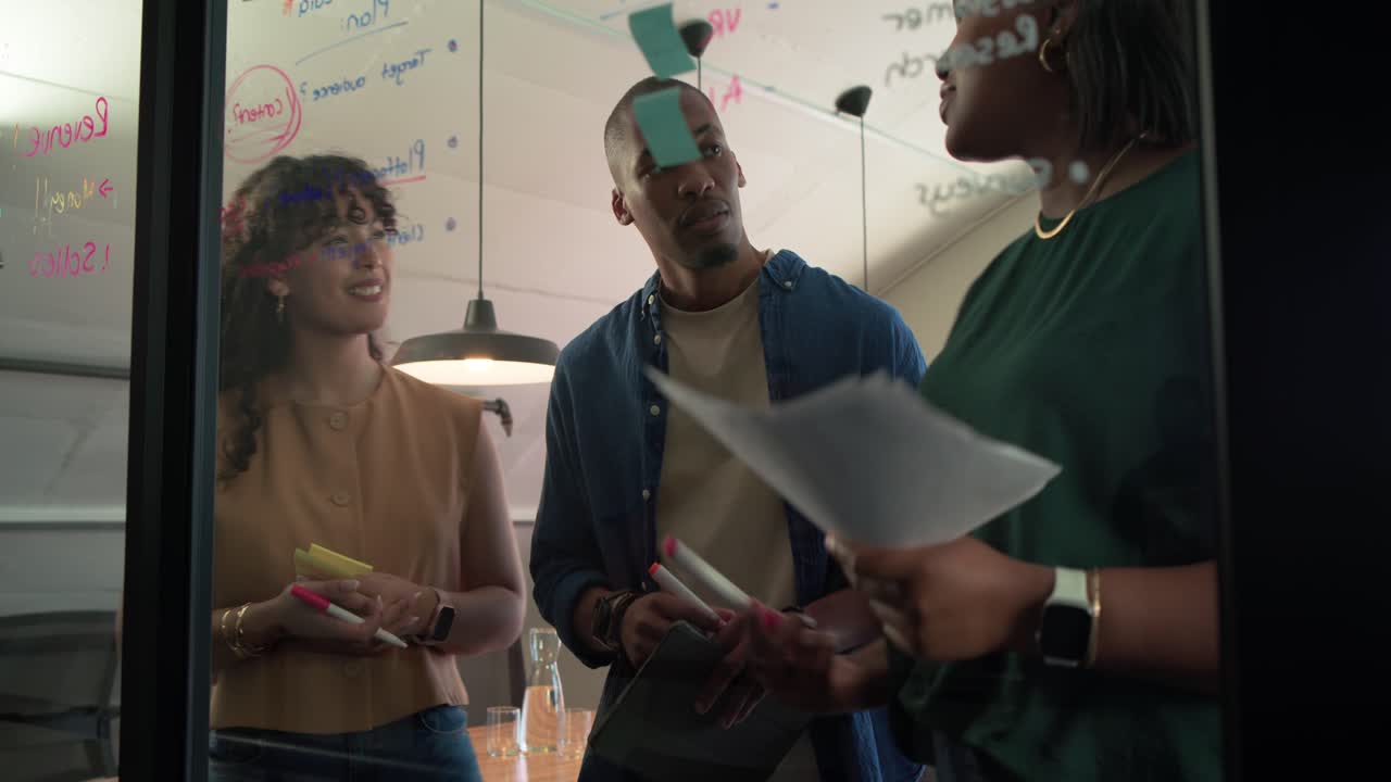 African American team aligning green sticky column on glass after pointing during office planning