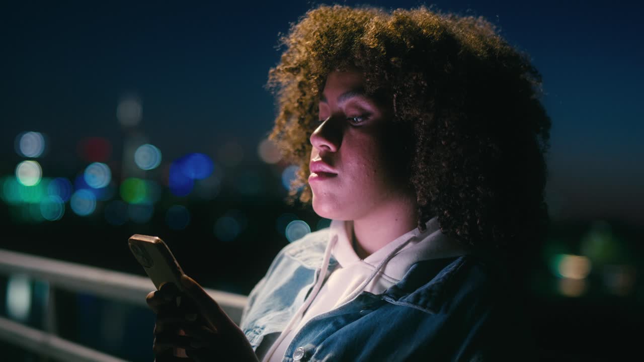 Black woman standing on the bridge at night and browsing her mobile phone