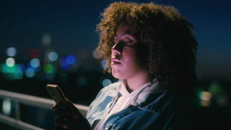 black woman standing on the bridge at night and browsing her mobile phone