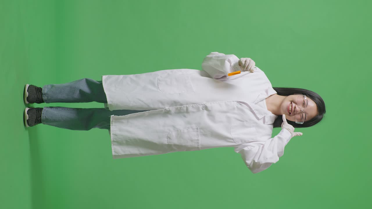 Full Body Of Asian Woman Scientist With Orange Liquid In The Test Tube Smiling And Making Call Me Gesture While Standing On The Green Screen Background In The Laboratory