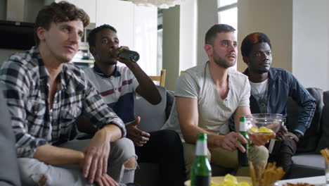 group of friends sitting on the couch eating snacks celebrate their team's victory while watching tv