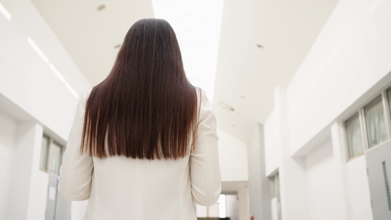 중년의 아름다운 아시아 사업가 여성이 사업 건물 사이를 걸어가며 기으로 미소 짓고 있습니다.