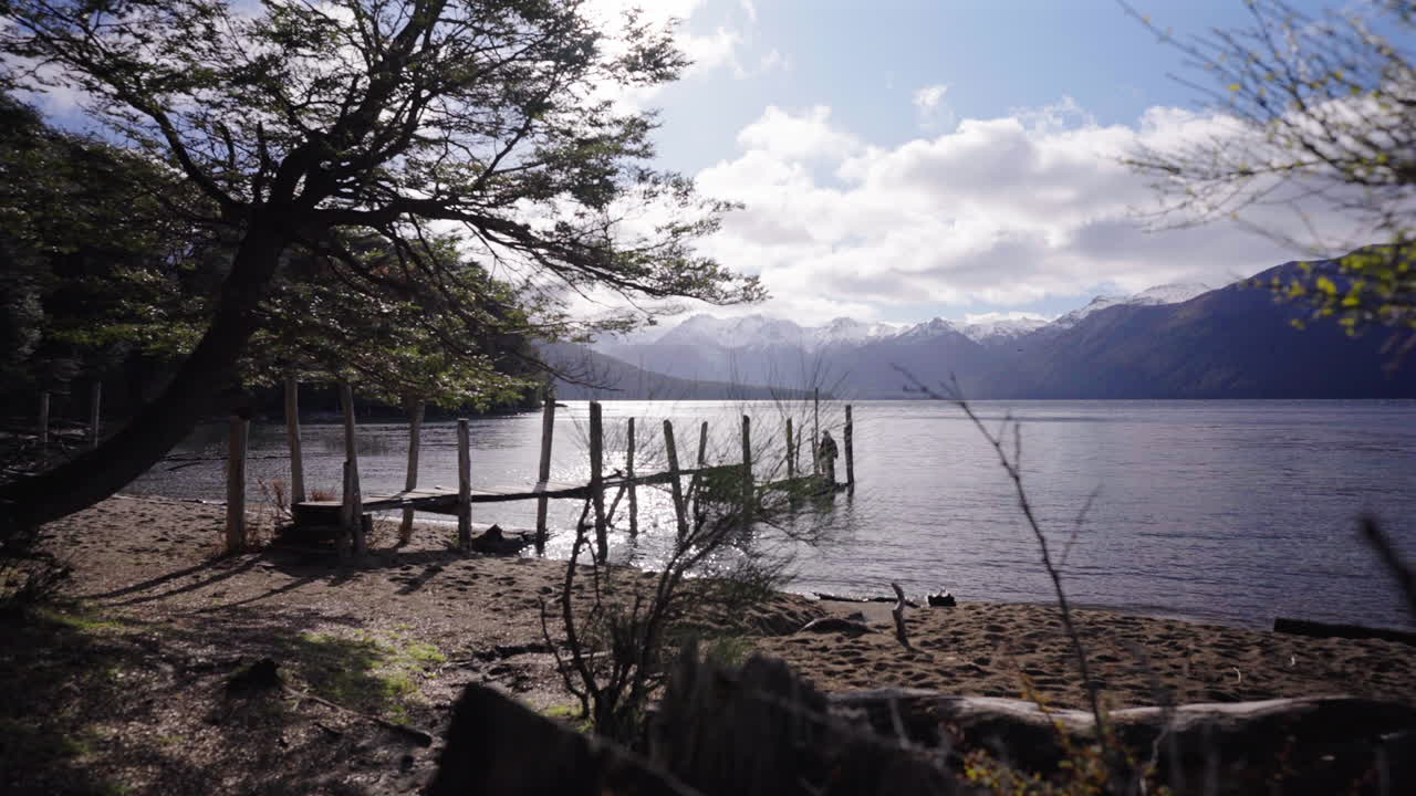 Mother and daughter on a rustic wooden pier under a dramatic cloudy sky with beautiful landscape at Lago Traful, Argentina