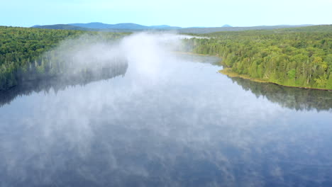 aerial drone shot rising above the fog and mist hanging above the still blue waters of the spectacle ponds in the maine wilderness