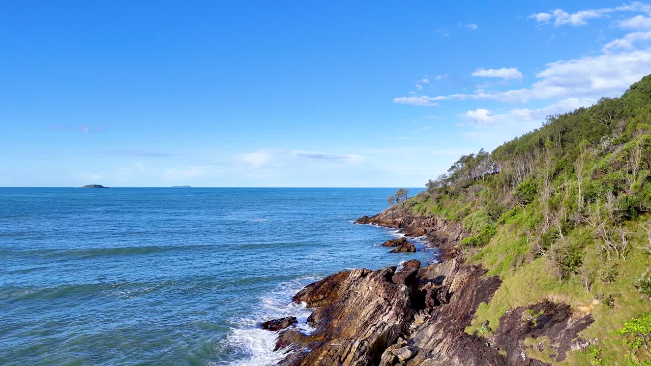 A serene coastal landscape with waves crashing against rocky cliffs under a clear blue sky at Charlesworth Bay Beach