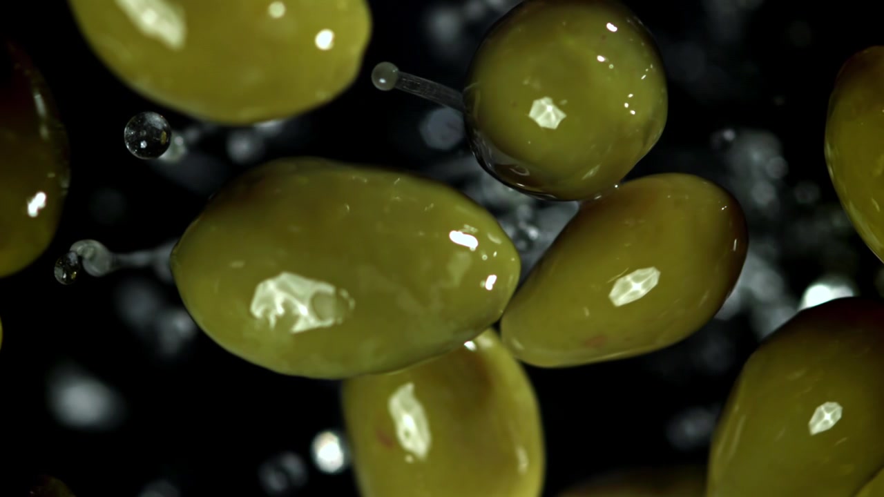 Olive verdi che cadono al rallentatore con gocce d'acqua su sfondo nero