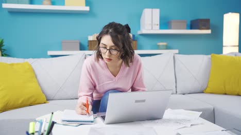 mujer joven trabajando desde casa tomando notas, trabajando en una computadora portátil.