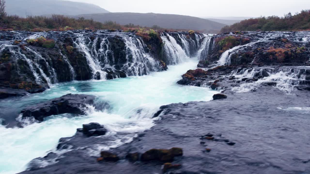 Aerial: Close flyover of Bruarfoss cascading waterfall off the golden circle in southern Iceland that's very picturesque with the beautiful blue cascade of falls into the plunge pool below