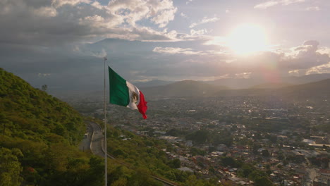 Real-Mexican-flag-waving-on-a-hill-in-a-Mexican-city-Oaxaca-at-dramatic-sunset