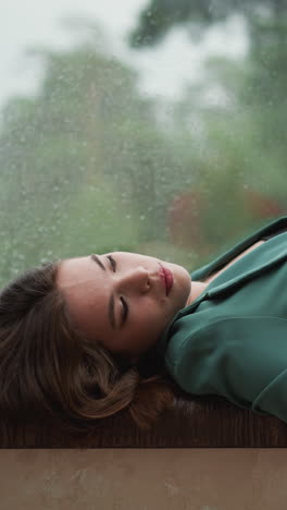 businesswoman leans back on windowsill. rainy weather helps to let go woman stresses plaguing mind. finding solace in sight of world beyond office walls