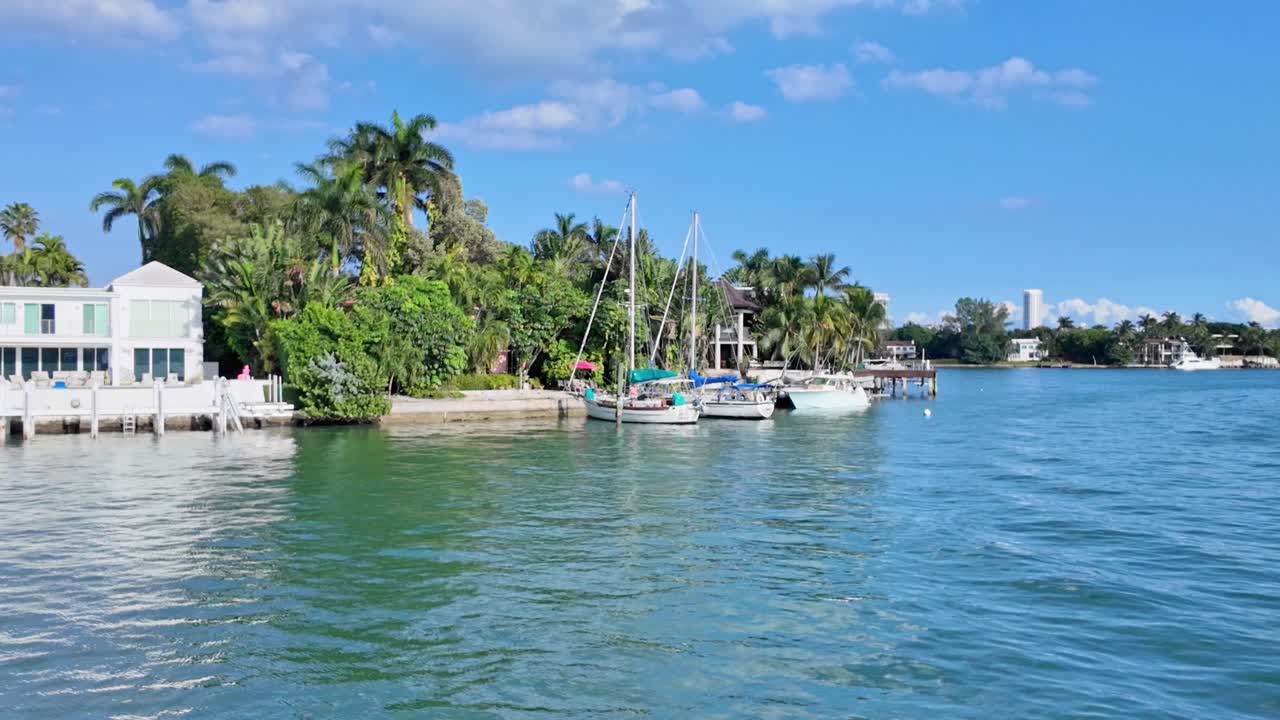 Aerial view of private villa at river with sailing boat at pier during sunny day in Miami, Florida - Establishing drone shot