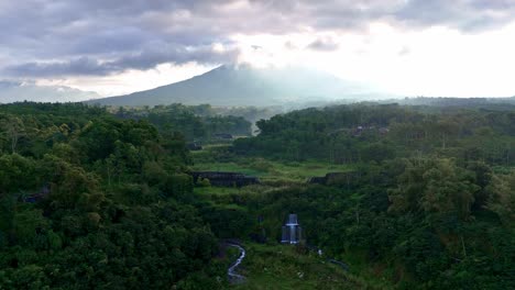 aerial nature landscape of rainforest vegetation with hidden waterfall and mountain background. slope of merapi volcano, indonesia.