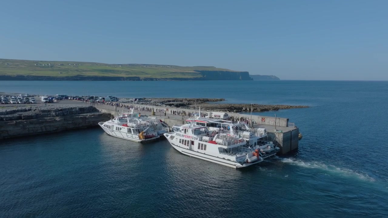 Packed Doolin harbor as two DoolinFerry.com vessels load summer tourists with the Cliffs of Moher coastline in the distance.