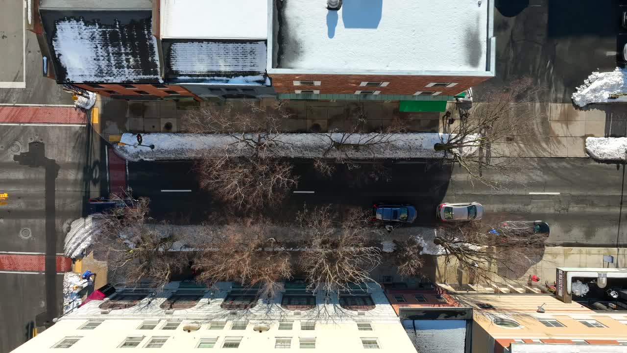 겨울철 불모의 나무가 있는 도시 거리 주변의 눈 덮인 집과 상점의 하향식 공중 전망