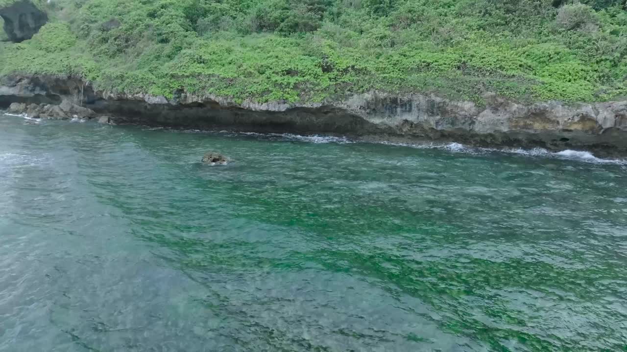 Slow Motion Drone View of Waves crashing over shallow coral reef and cliff coastline in Uluwatu Bali Indonesia