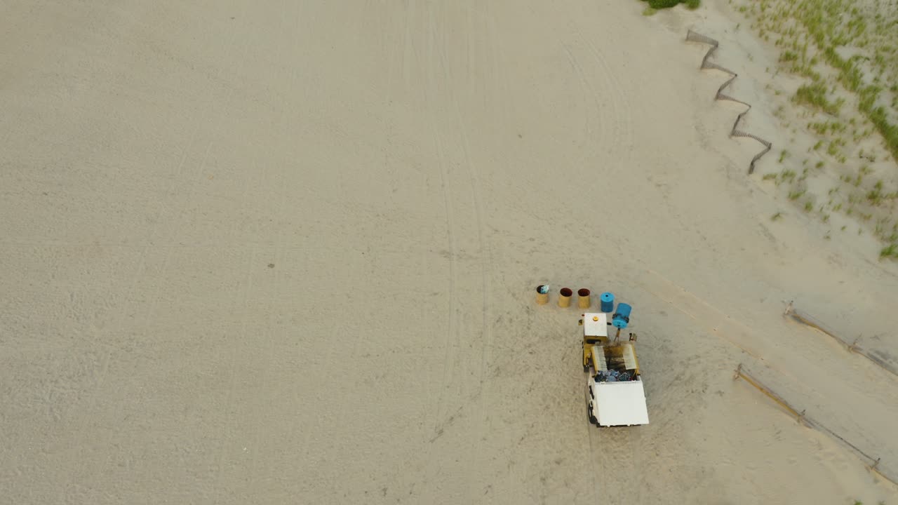 Aerial tracking garbage buggy on beach picking up and emptying garbage bins