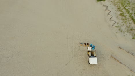 aerial tracking garbage buggy on beach picking up and emptying garbage bins