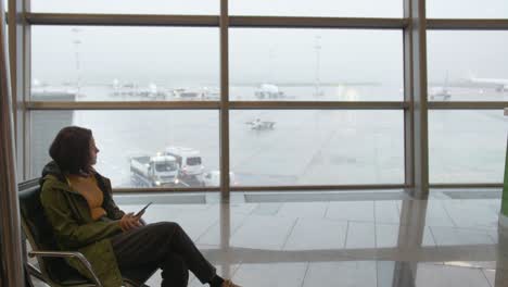a young woman in a yellow jacket and a green raincoat sits alone at the airport