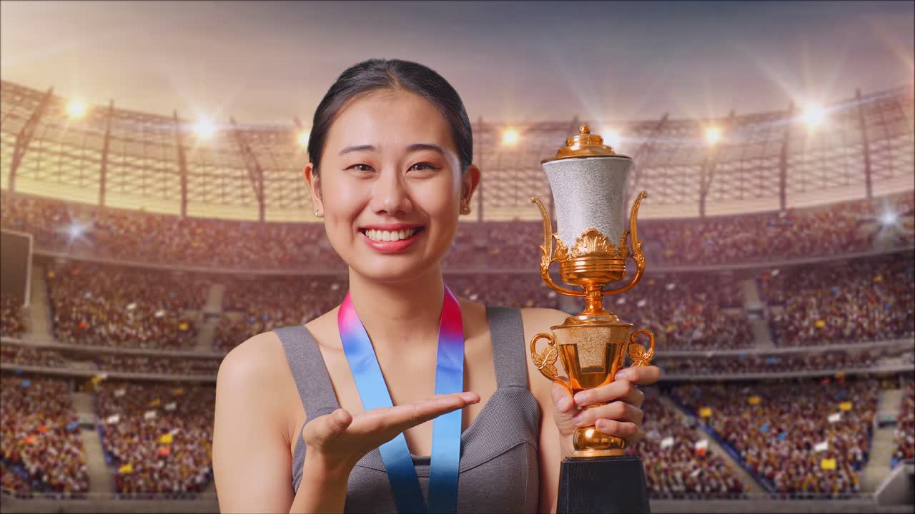 Close Up Of Asian Woman With A Gold Medal Pointing To A Gold Trophy In Her Hand And Smiling Being Proud Winning As The First Winner At The Stadium