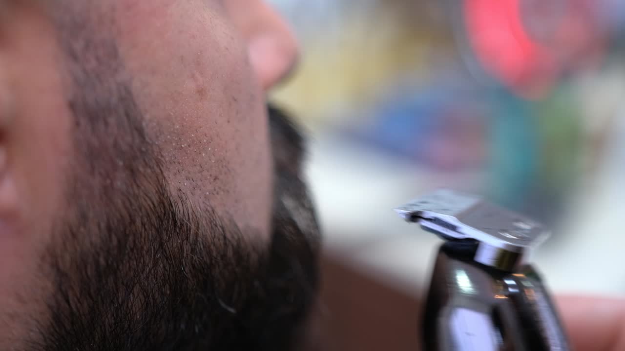 un barbero utiliza una recortadora eléctrica para limpiar la barba de un cliente