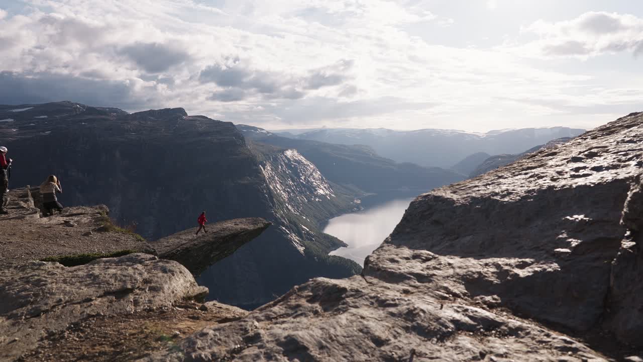 Hiker standing on Trolltunga rock ledge in Norway, overlooking fjord and mountains