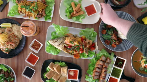 male hand picking up thai cuisine fried tofu pieces from flat lay food arrangement