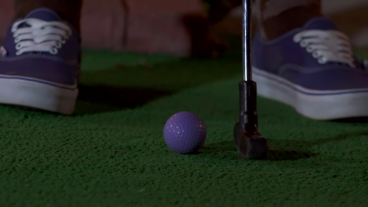 A close up of a purple mini golf ball getting hit with a club