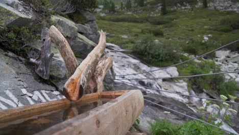 Una-Fuente-De-Madera-En-Primer-Plano-Y-Un-Río-Que-Corre-Por-Una-Montaña-En-El-Fondo