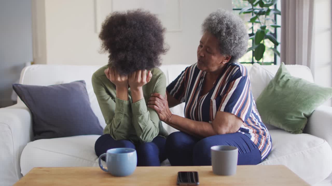 African american senior mother comforting sad, crying adult daughter at home, slow motion