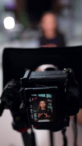positive energetic caucasian lady in black jacket talks on the display of professional camera. high angle view at the equipment recording a blog. vertical video.