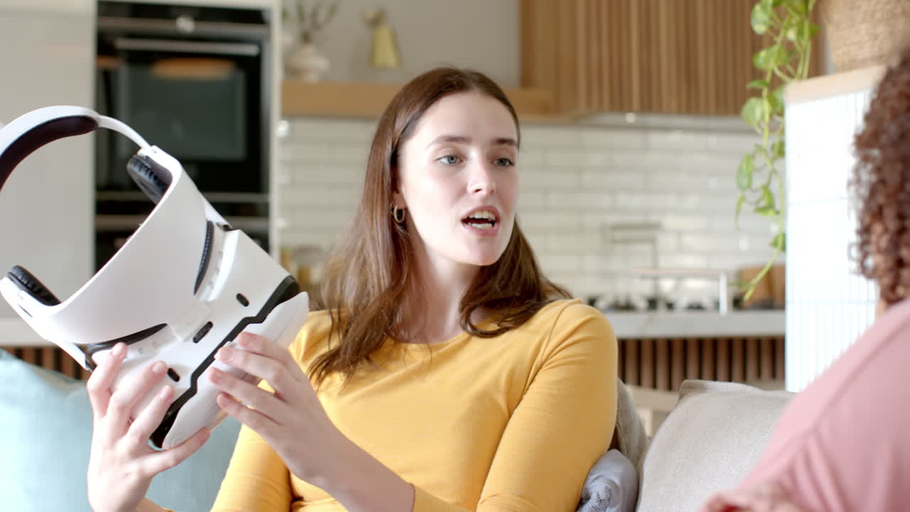 Holding VR headset, woman sitting on couch talking to friend at home