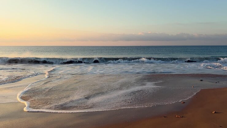 The cinematic scene of the seaside, where sea waves gently kiss the shore in the evening, reveals the vastness of the ocean surface