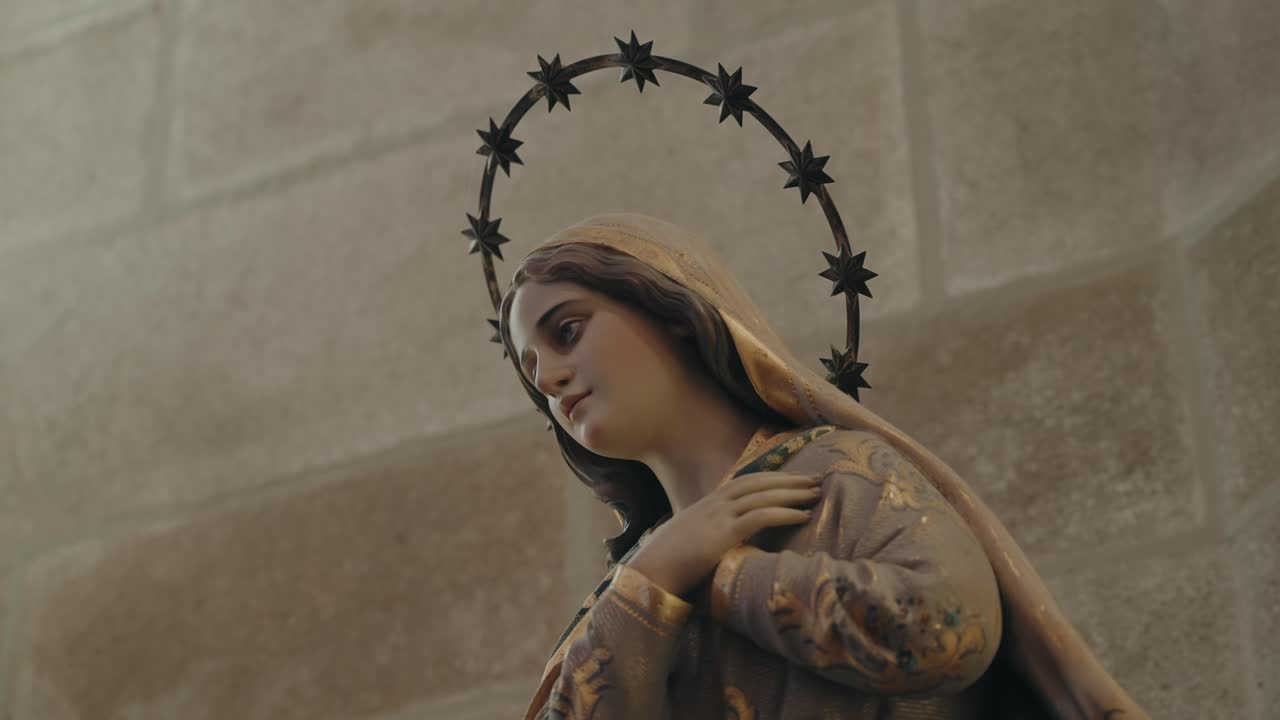 Virgin Mary statue with halo of stars and folded hands inside historic church setting